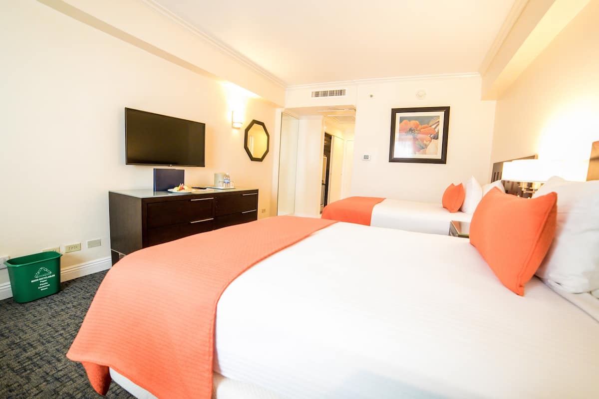 Une chambre d’hôtel avec deux lits, un téléviseur à écran plat, un bureau et une poubelle verte pour le recyclage.