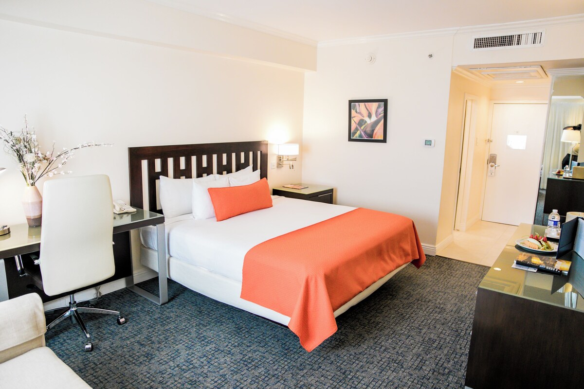Une chambre d’hôtel comprenant un lit, un bureau avec une chaise, une table de chevet et une petite table avec une lampe.
