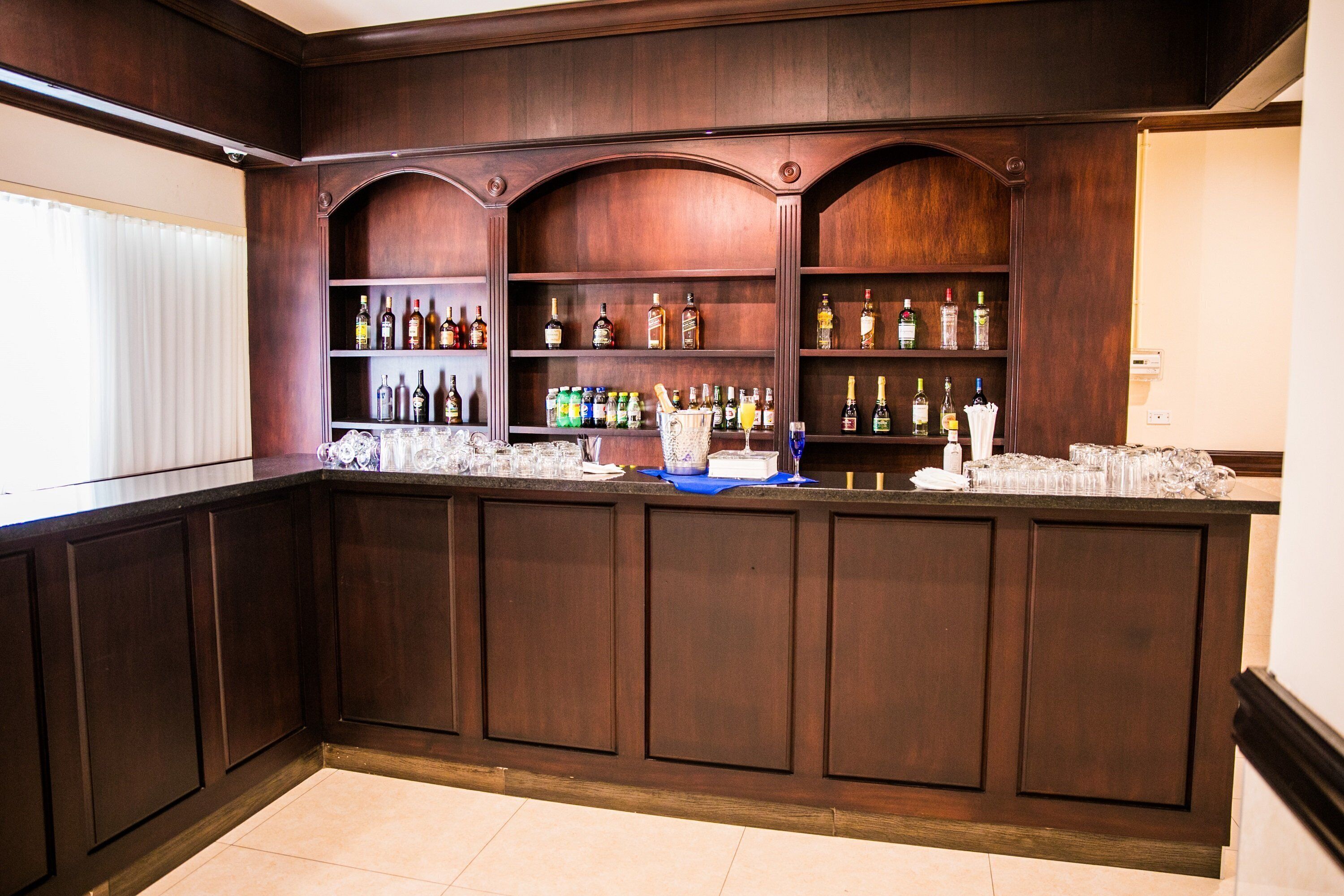 A bar area with wooden paneling and shelves stocked with various bottles and glasses.