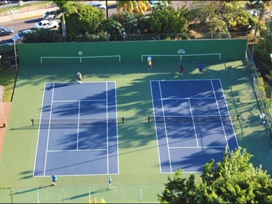 An outdoor tennis court with two courts, surrounded by trees and a fence.