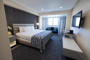 Una camera d'hotel con un letto grande, una scrivania, una sedia, una televisione e una finestra con tende.