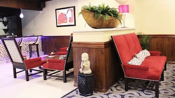 A lobby with red upholstered chairs, a wooden planter with greenery, a statue, and a patterned carpet.