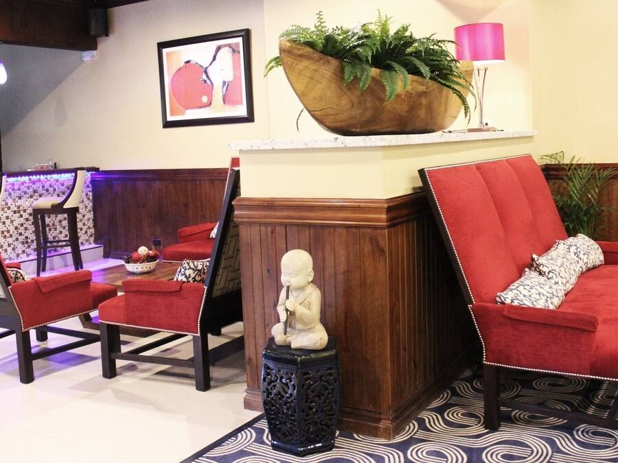 Un hall d’entrée avec des fauteuils à revêtement rouge, un bac à fleurs en bois orné de plantes vertes, une statue et un tapis à motifs.