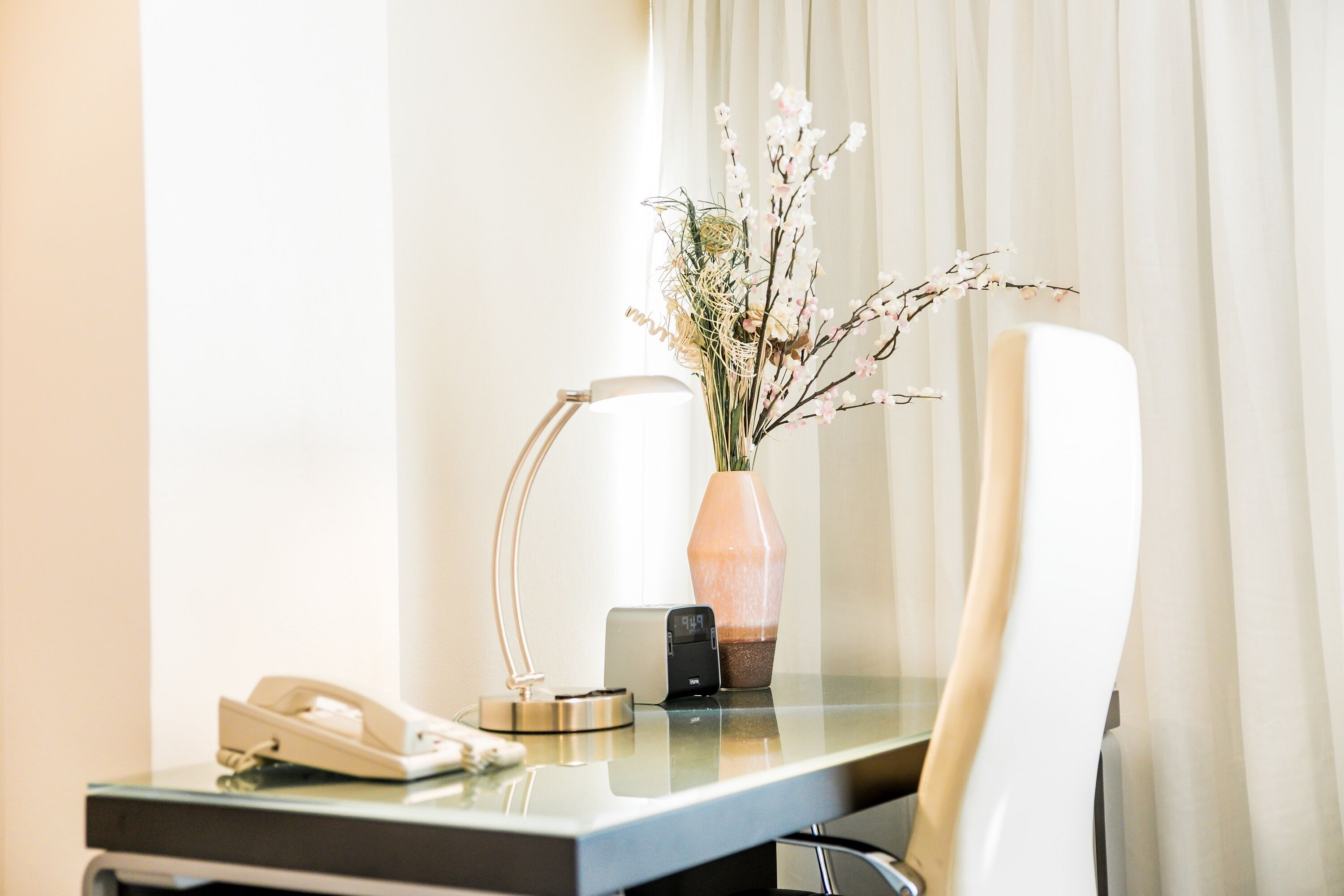 Balcão de hotel com um telefone, uma luminária e um vaso com flores.