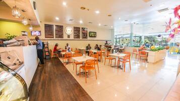 A restaurant with multiple tables and chairs, a counter with a person at the front, and menu boards on the wall.