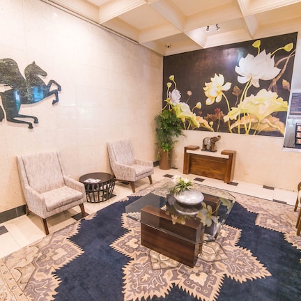 A lobby with a marble wall, a mural of flowers, a decorative horse sculpture, and a seating area with sofas and a coffee table.