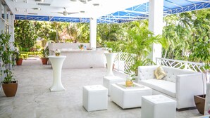 A covered outdoor lounge area with white furniture, potted plants, and a view of the surrounding greenery. - The Jamaica Pegasus Hotel (Kingston)