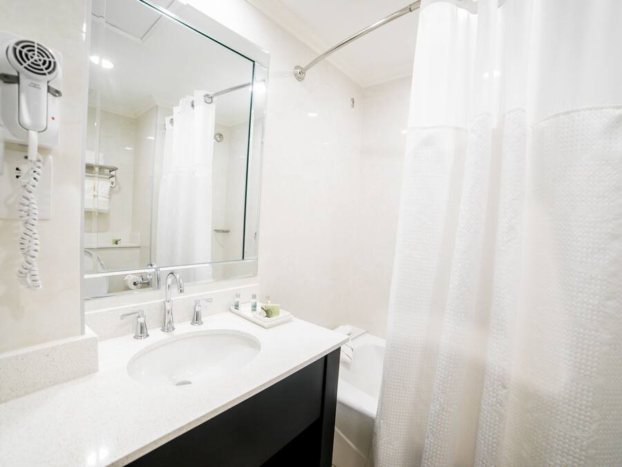 Un baño con lavamanos blanco, un espejo, secador de pelo y cortina de ducha.