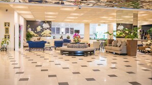 A spacious lobby with a checkered floor, a blue sofa, a round seating area, and a wall with floral decorations. - The Jamaica Pegasus Hotel (Kingston)