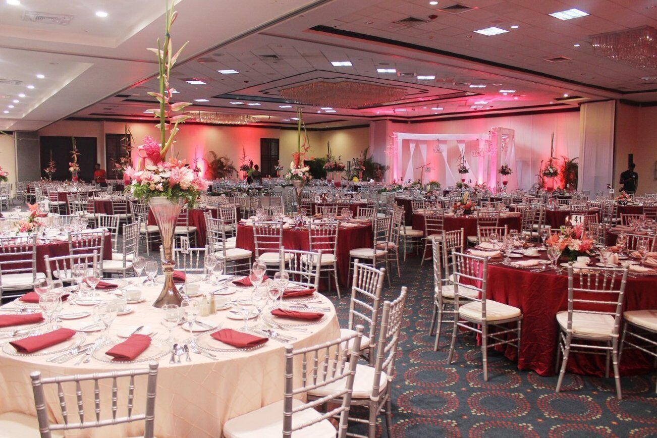 A banquet hall with round tables set for dining, each with white chairs and red tablecloths.