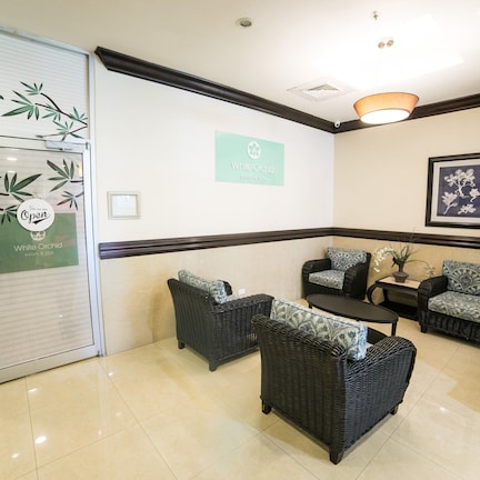 A reception area with wicker furniture, a sign for 'White Orchid', and a tiled floor.