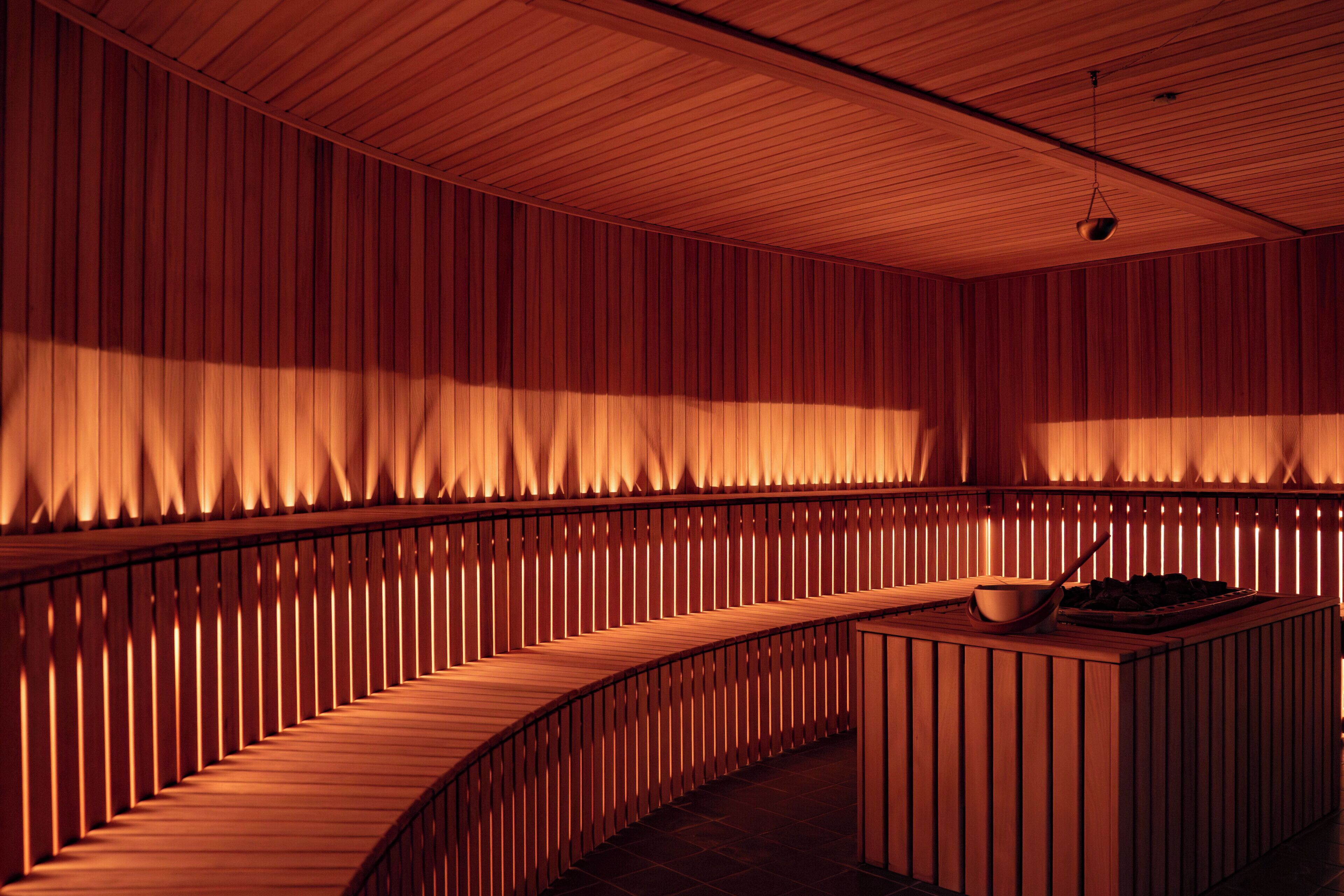 A room with a curved wooden bench, a small table with a bowl, and vertical wooden slats on the walls.