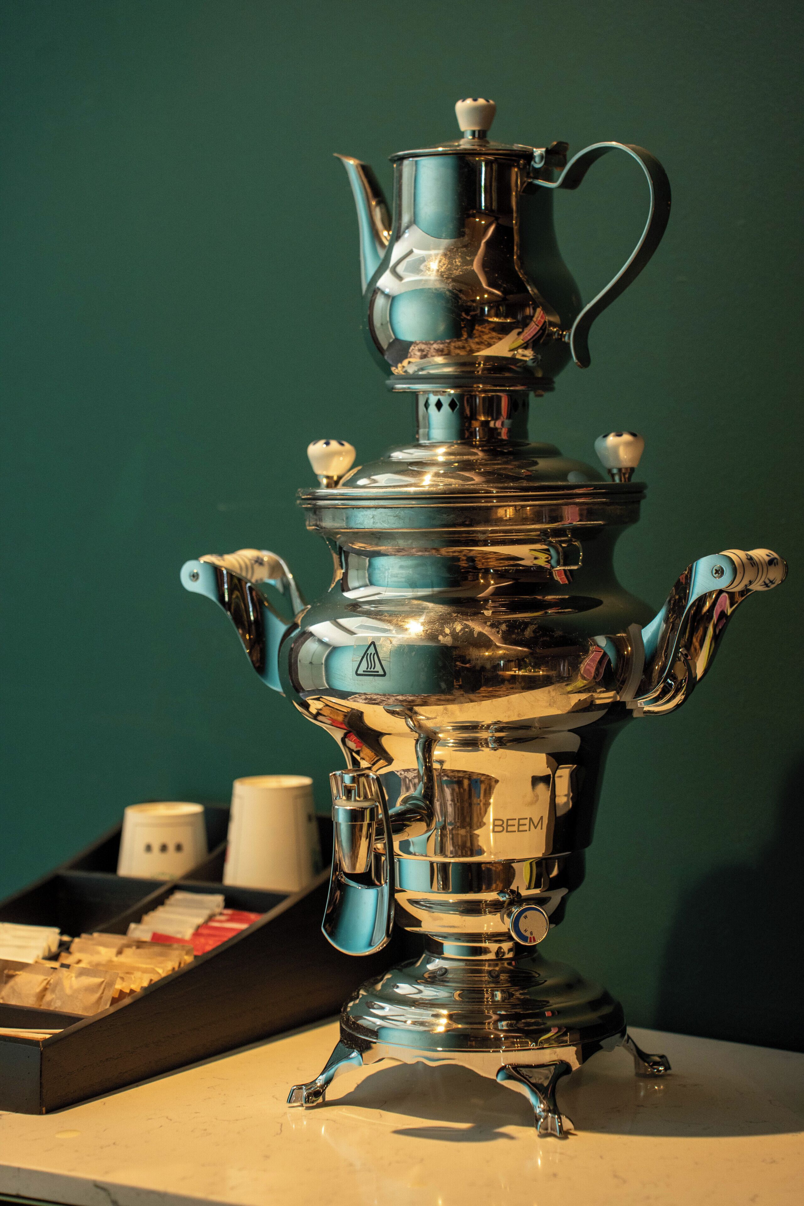 A traditional Russian samovar with a kettle on top, a tray with tea bags, and a white cup in the background.