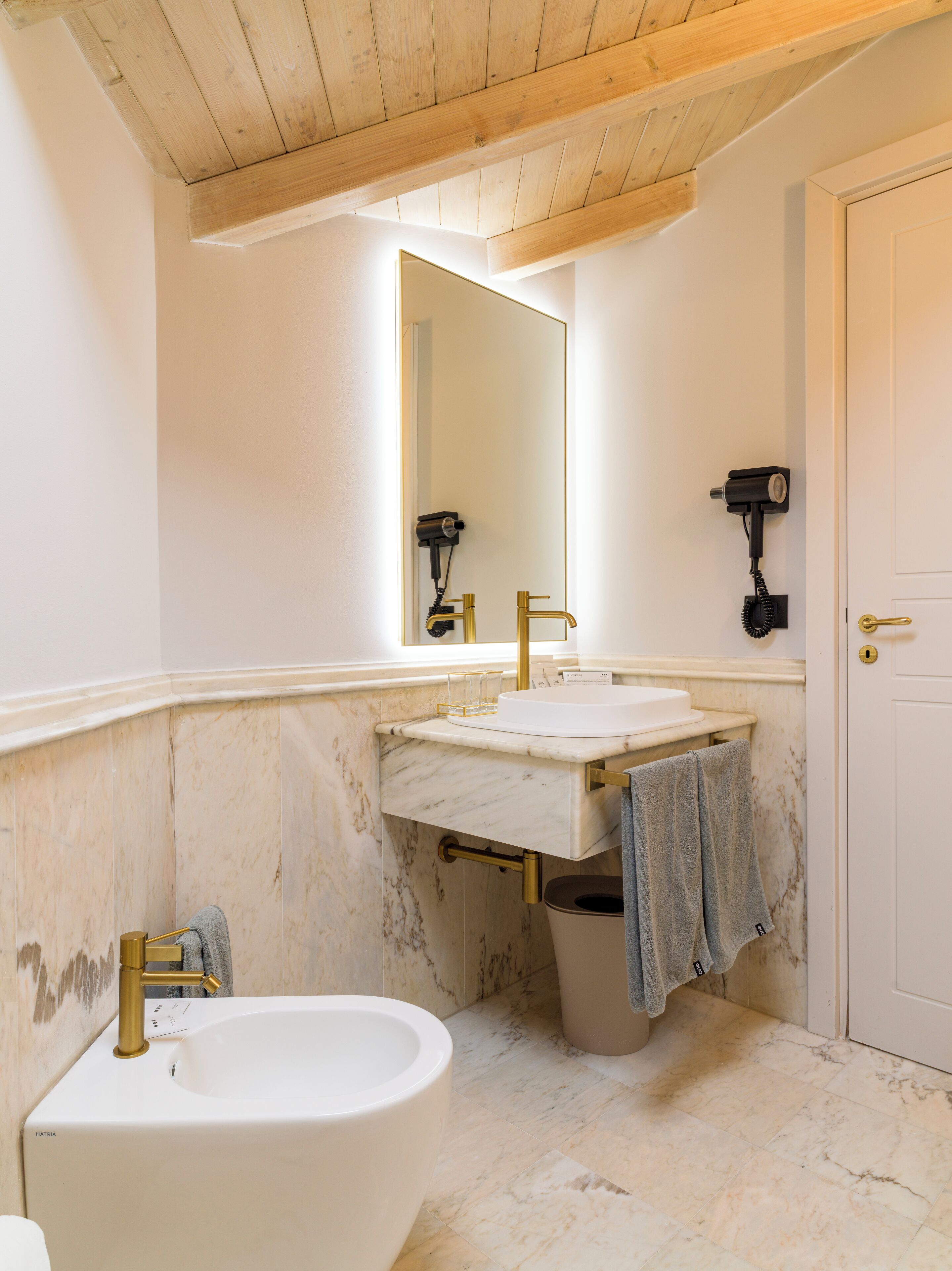 Ein Badezimmer mit Marmorwaschtisch, einem weißen Waschbecken, einem goldfarbenen Wasserhahn, einer Badewanne und einem Spiegel über dem Waschtisch.