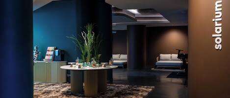 A modern lobby with a reception desk, a round table with decorative items, a sofa, and a wall with the text 'solarium'.