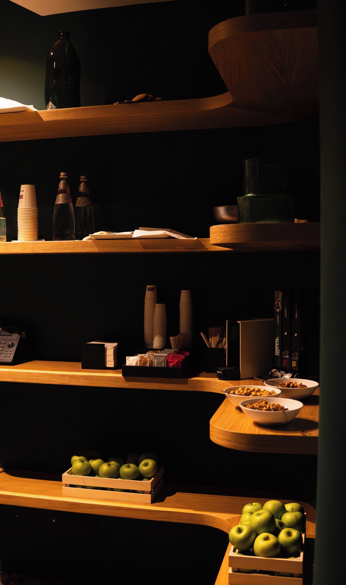 A dimly lit room with wooden shelves containing various items such as bottles, bowls, and a tray with apples.
