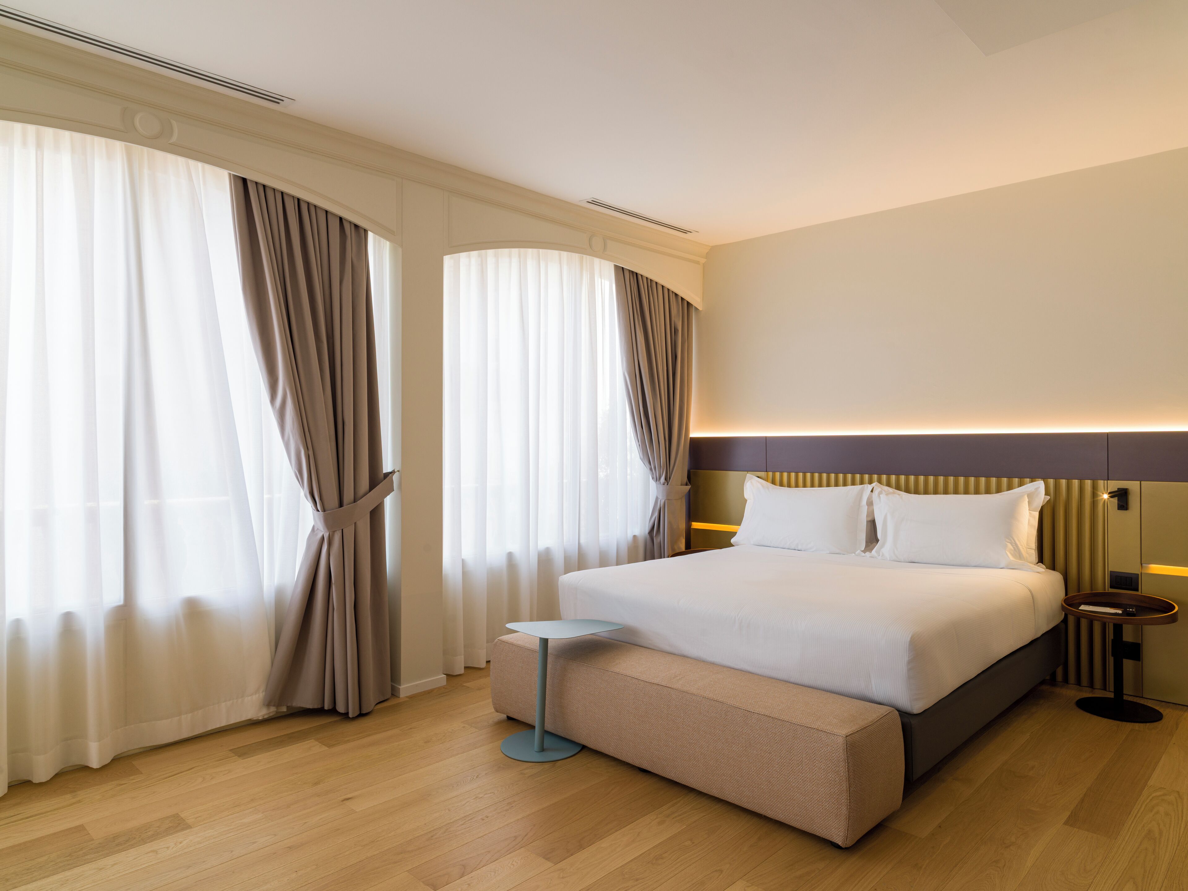 Una habitación de hotel moderna con una cama grande, una mesita de noche y una pequeña mesa redonda.