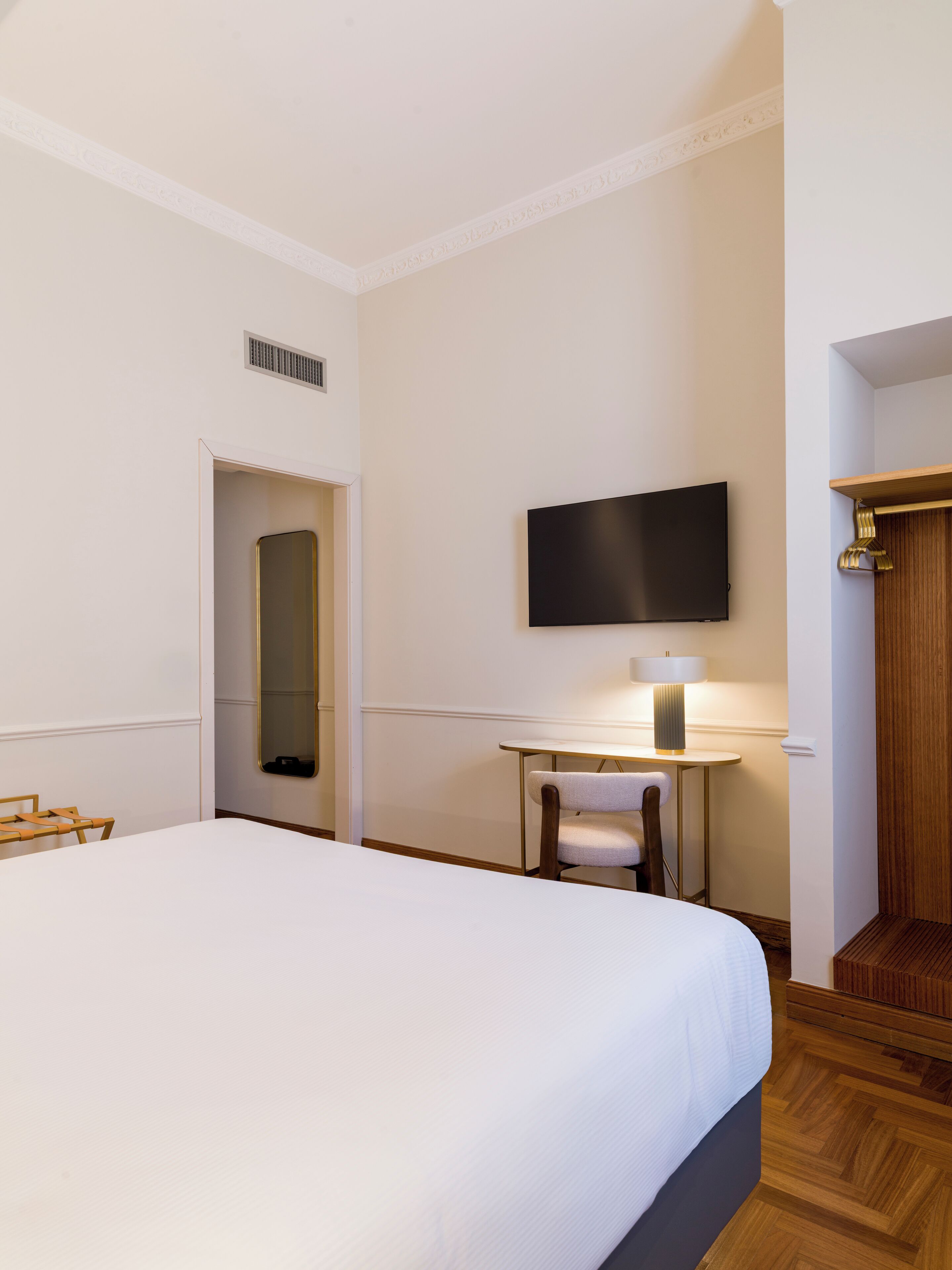 Una camera d'albergo con un letto grande, una scrivania con sedia, una TV a schermo piatto montata a parete e un armadio in legno.