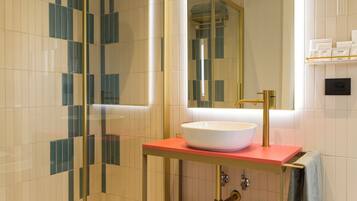 Un bagno moderno con doccia vetrata, lavandino bianco su un piano di lavoro rosso, rubinetto dorato e specchio sopra il lavandino.