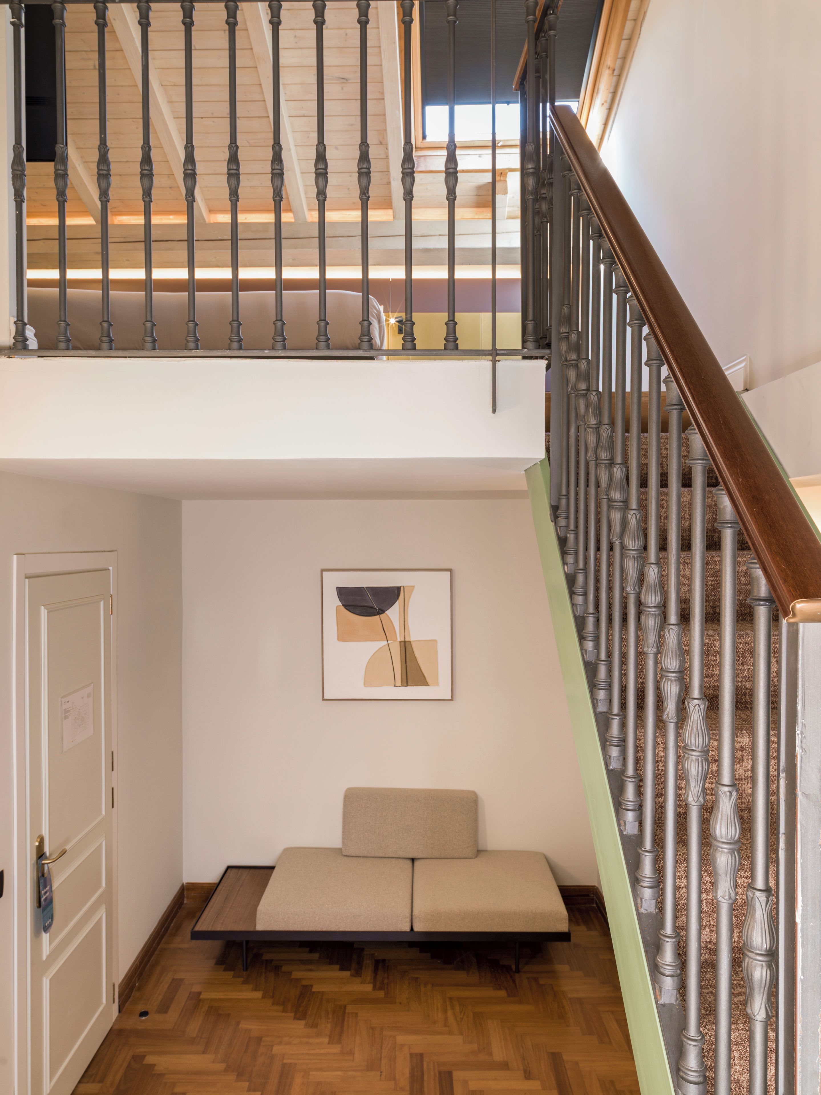 Une pièce de style « loft », avec un plancher en bois, un canapé, un tableau et un escalier doté d’une rampe en bois.