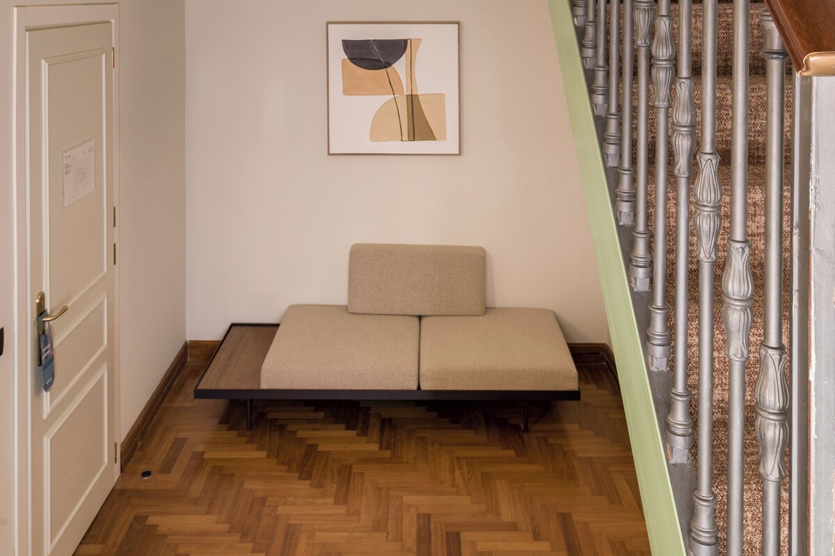 Un cuarto estilo loft con piso de madera, un sofá, un cuadro y una escalera con barandilla de madera.