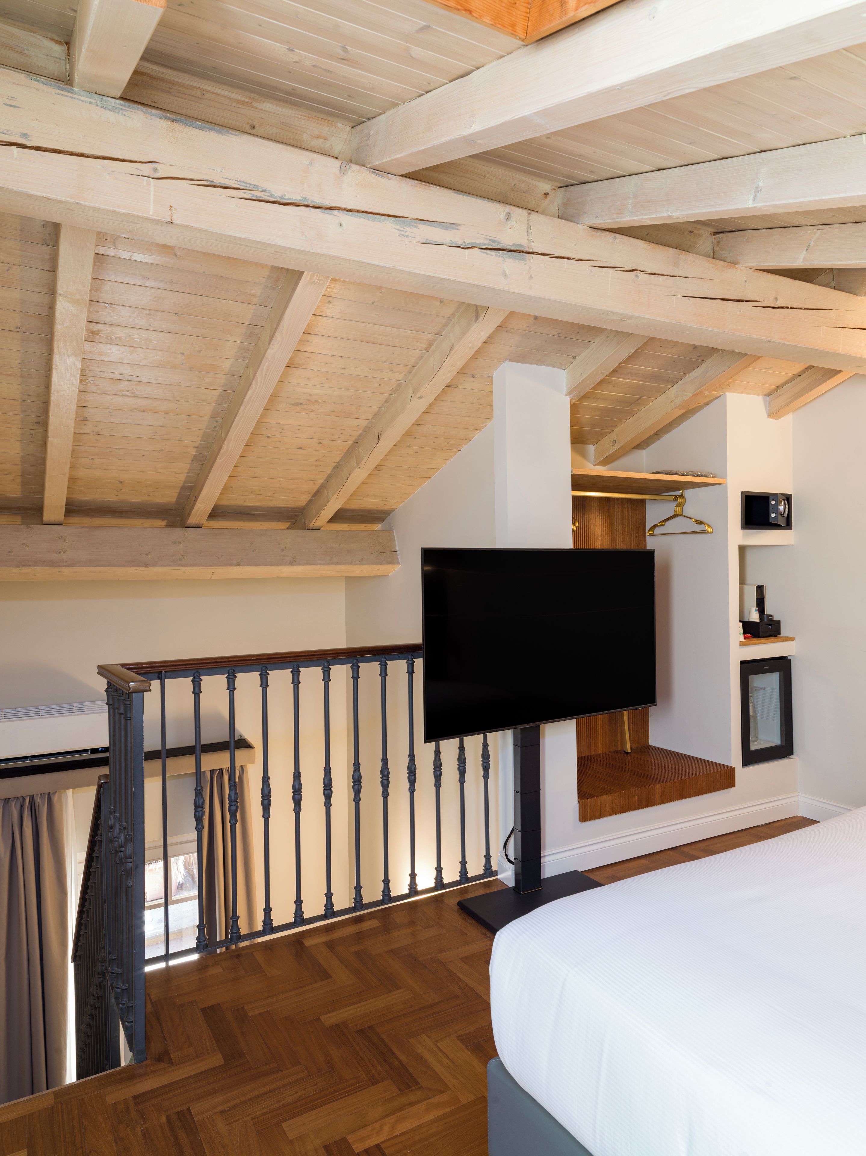 Una camera da letto con soffitto in legno, un letto, una TV e una piccola mensola.