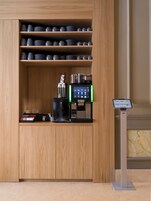 Un mobiletto in legno con ripiani che ospitano piatti e tazze, una macchina da caffè e un piccolo espositore.