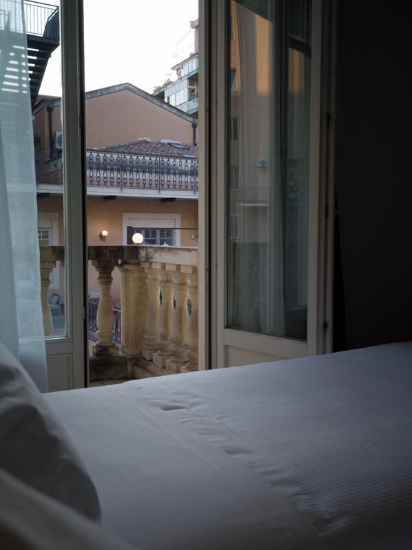 A hotel room with a bed, a view of a courtyard with a balcony, and a building with a tiled roof. - UNA Hotels One Catania Wellness & SPA (Catania)