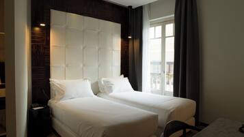 A hotel room with two beds, a dark wood headboard, a large window with curtains, and a small table.