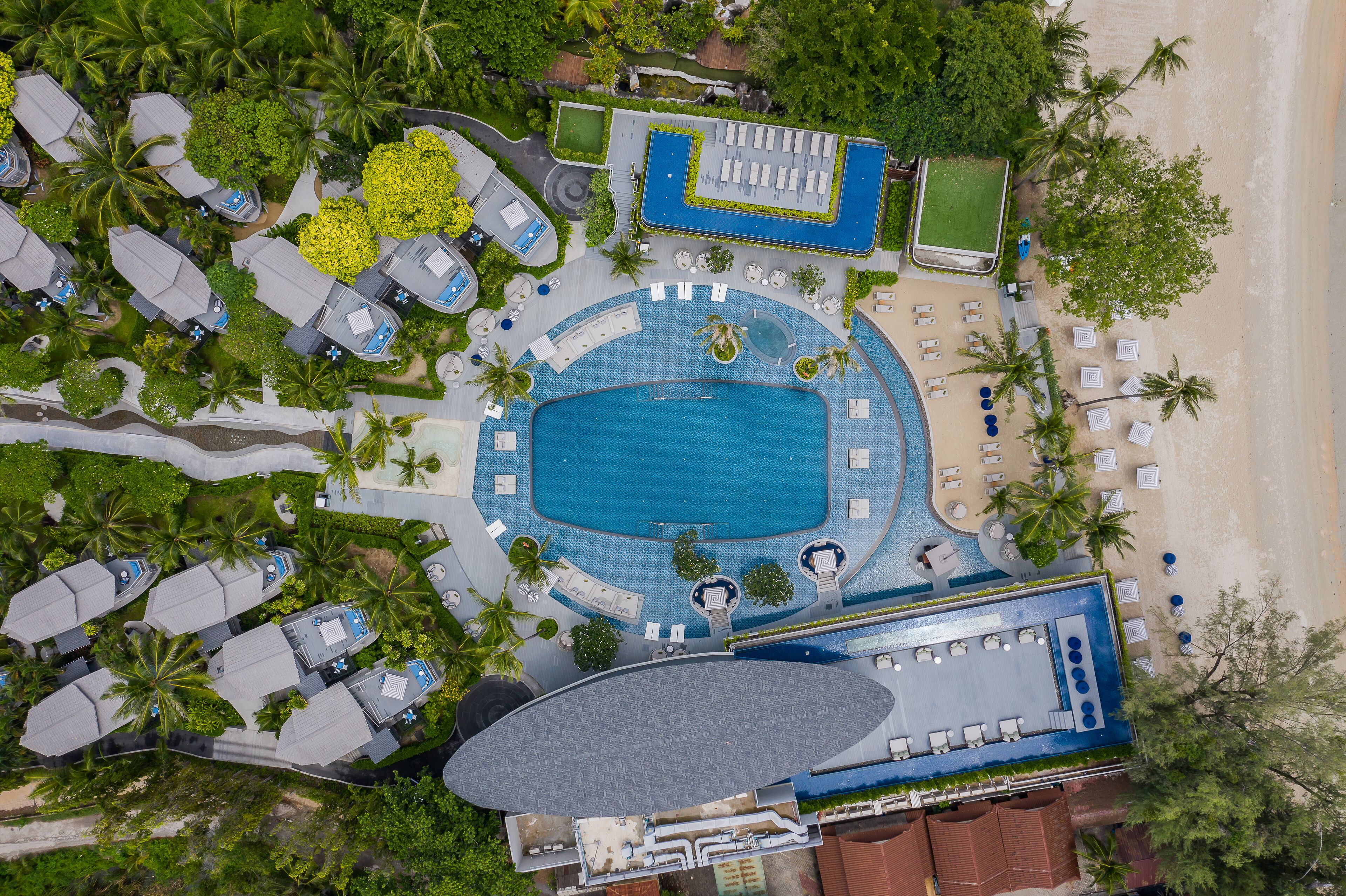Vista aérea de un complejo turístico con una piscina central, varias zonas de descanso y una playa.