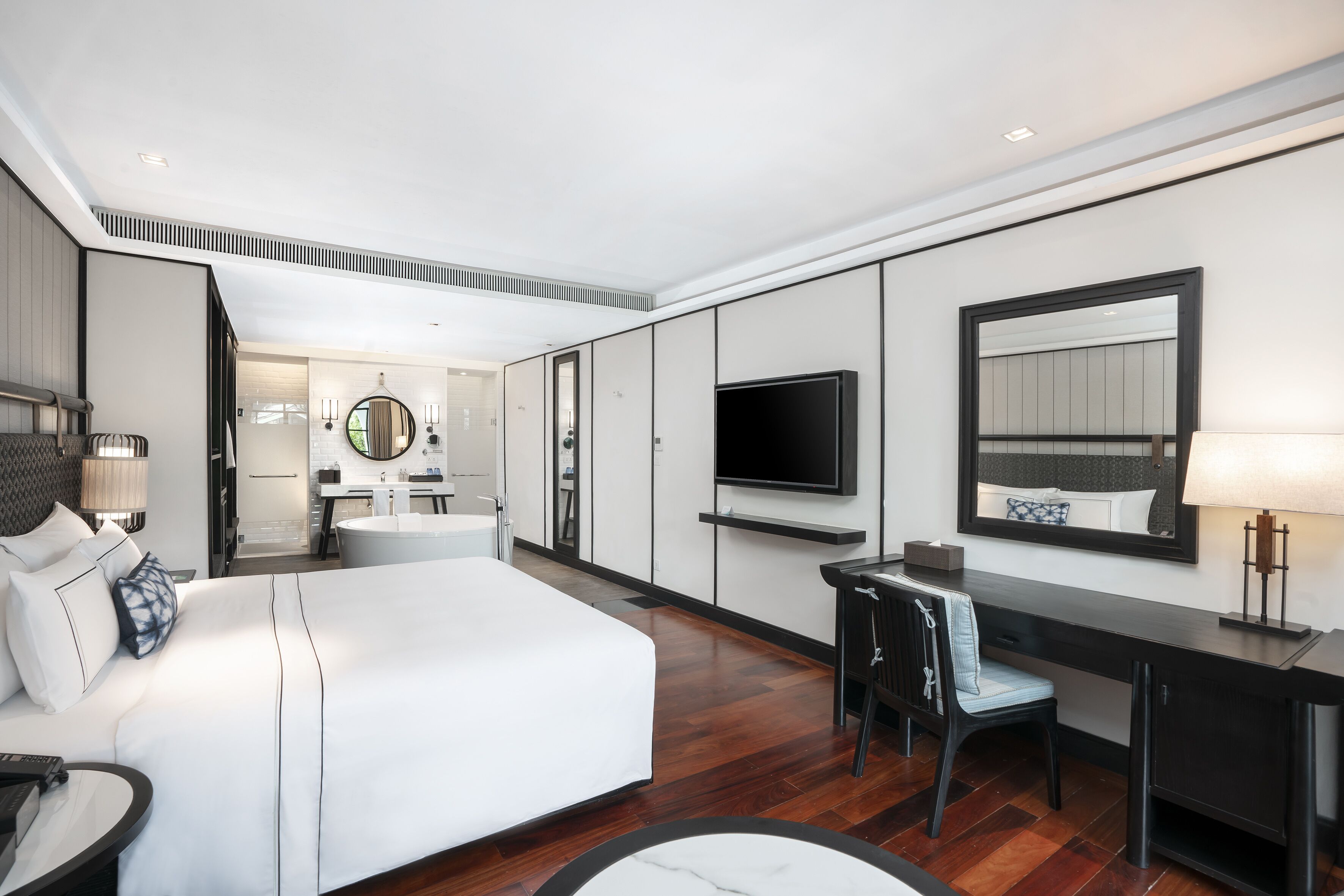 Una habitación de hotel moderna con una cama grande, un escritorio, un televisor y un baño visible al fondo.