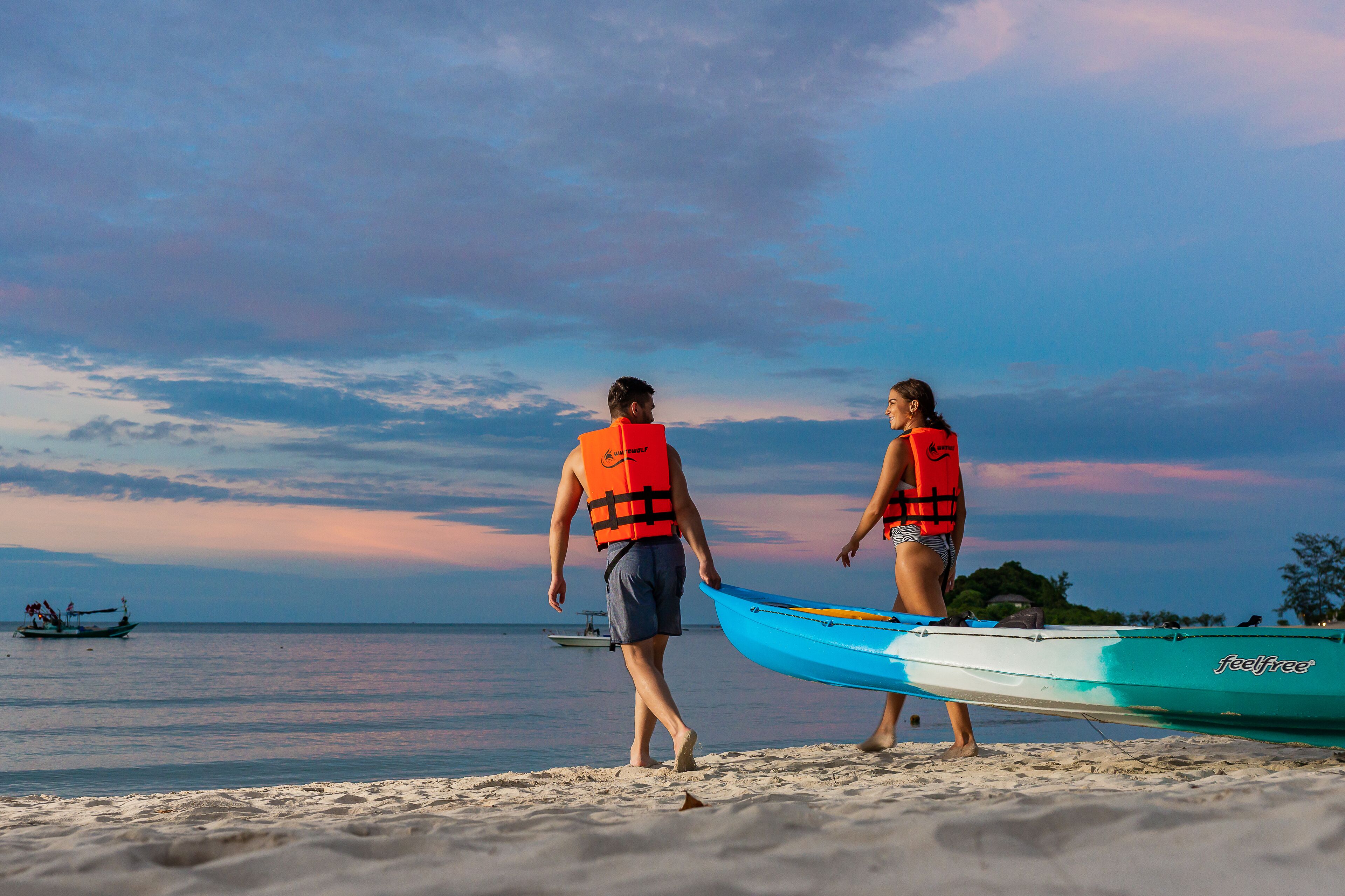 Two people walking on a beach with a kayak and a boat in the background.