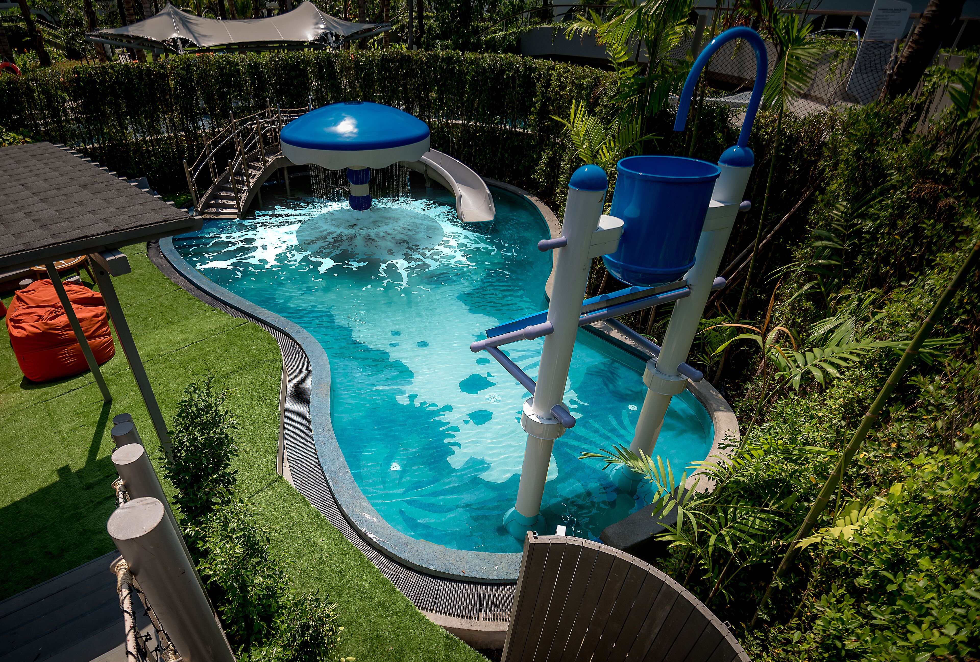 A swimming pool with a water slide, surrounded by lush greenery and a covered seating area.