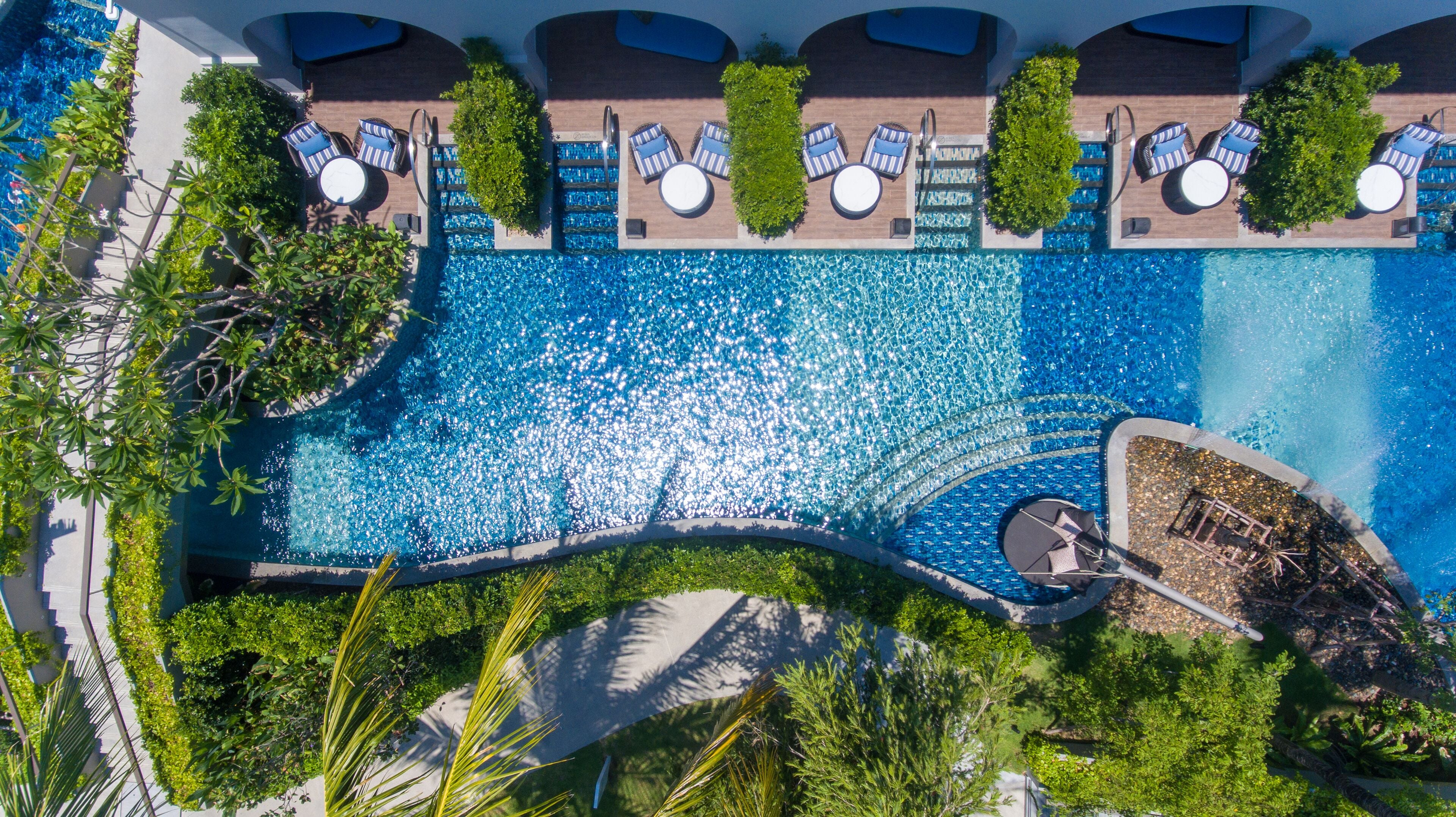 An aerial view of a hotel pool area with multiple lounge chairs and a small waterfall feature.