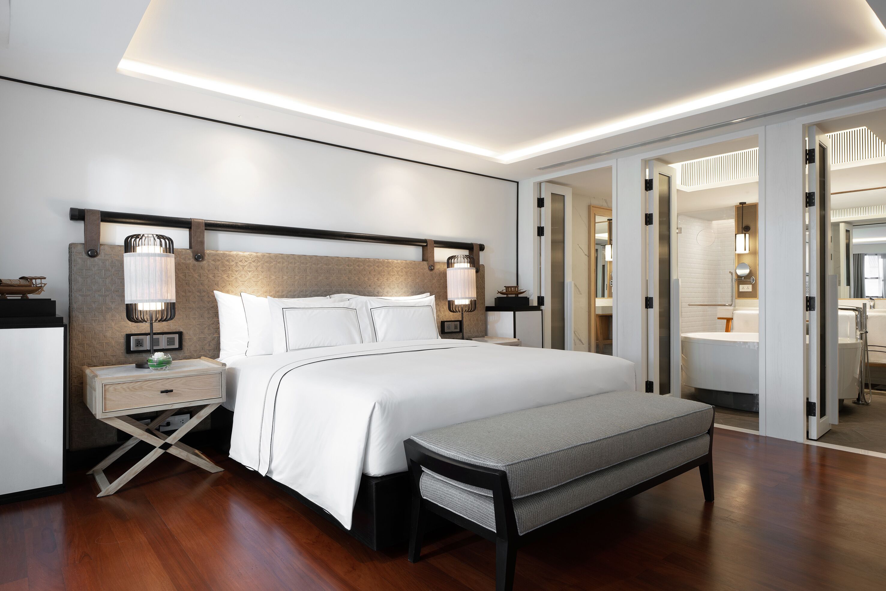 Una habitación de hotel moderna con una cama grande, mesitas de noche, un banco y un vestidor.