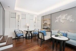 A modern living room with a wooden floor, a sofa, two chairs, a small table, and a decorative wall piece.