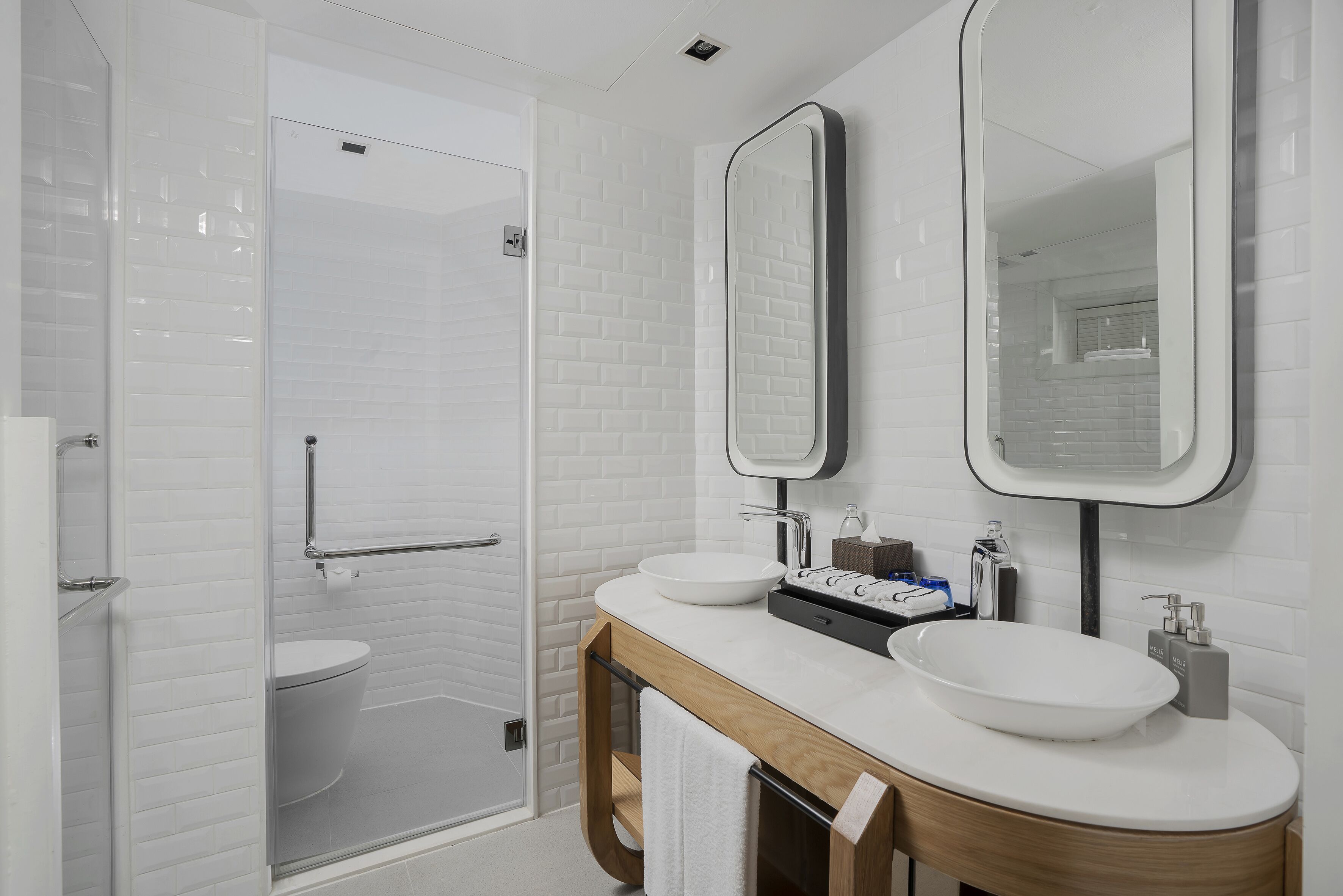 Une salle de bain moderne avec une douche à parois de verre, des toilettes blanches et deux lavabos avec miroirs.