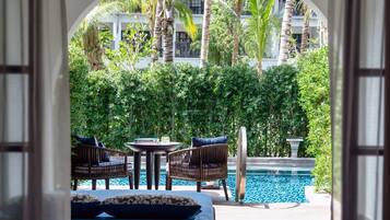 An outdoor seating area with wicker chairs and a table, overlooking a pool with blue tiles.