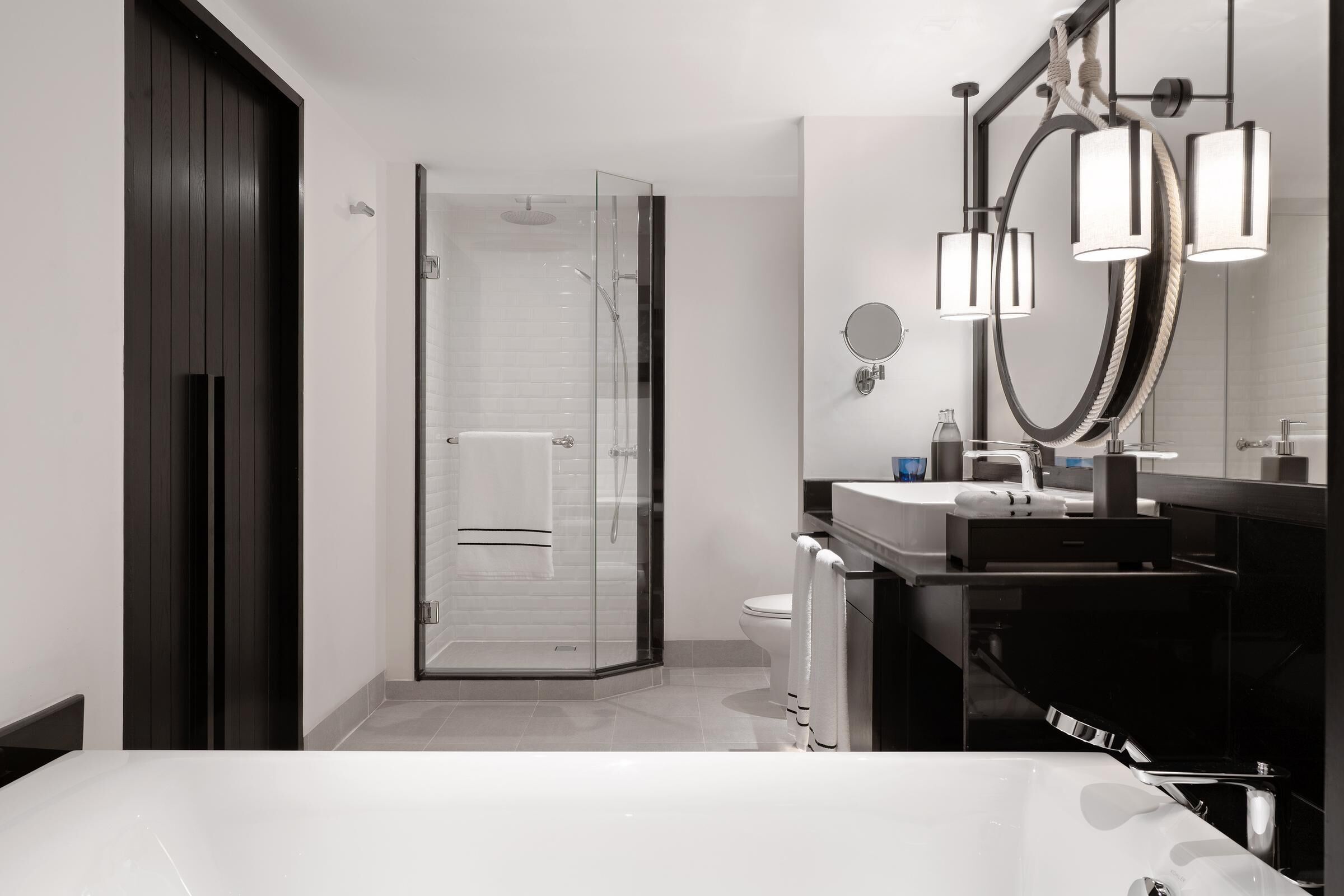 Une salle de bain moderne avec une douche à parois de verre, un grand miroir et une baignoire blanche.