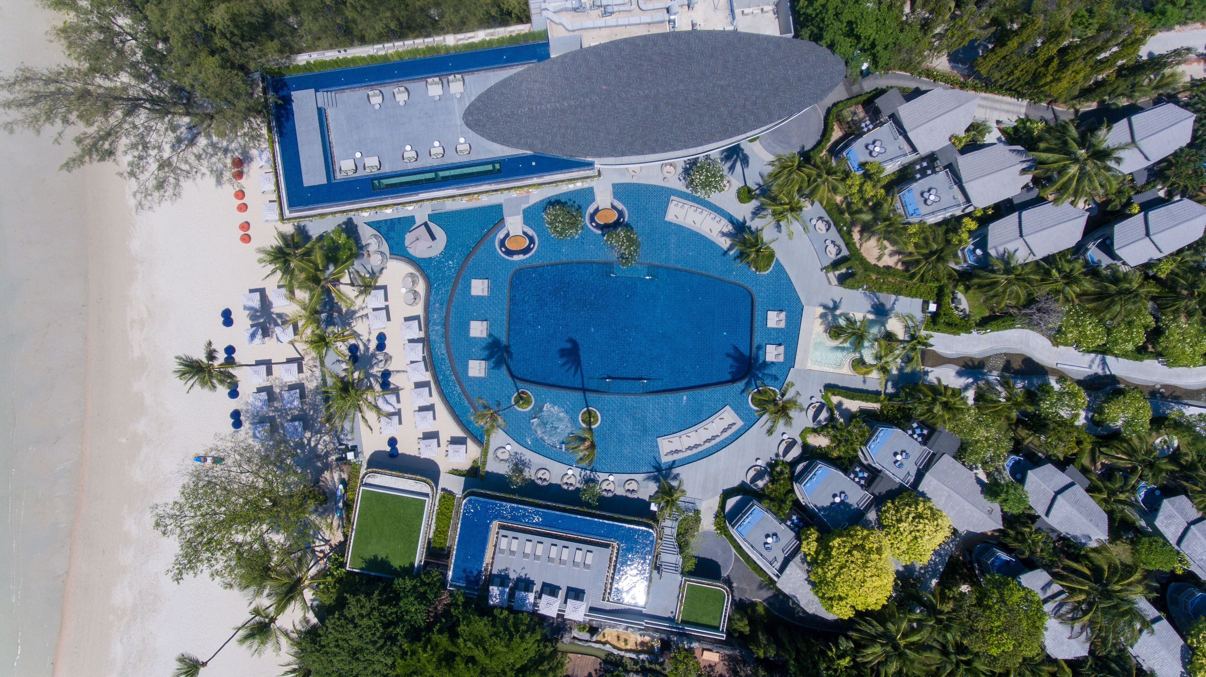 An aerial view of a resort with a large central pool, multiple lounge areas, and a beachside location.