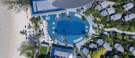 An aerial view of a resort with a large central pool, multiple lounge areas, and a beachside location.