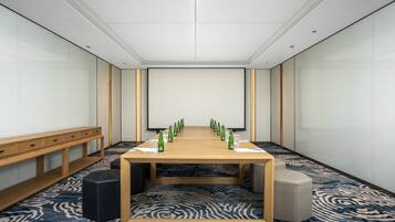 A conference room with a long table, chairs, a projector screen, and a carpeted floor.