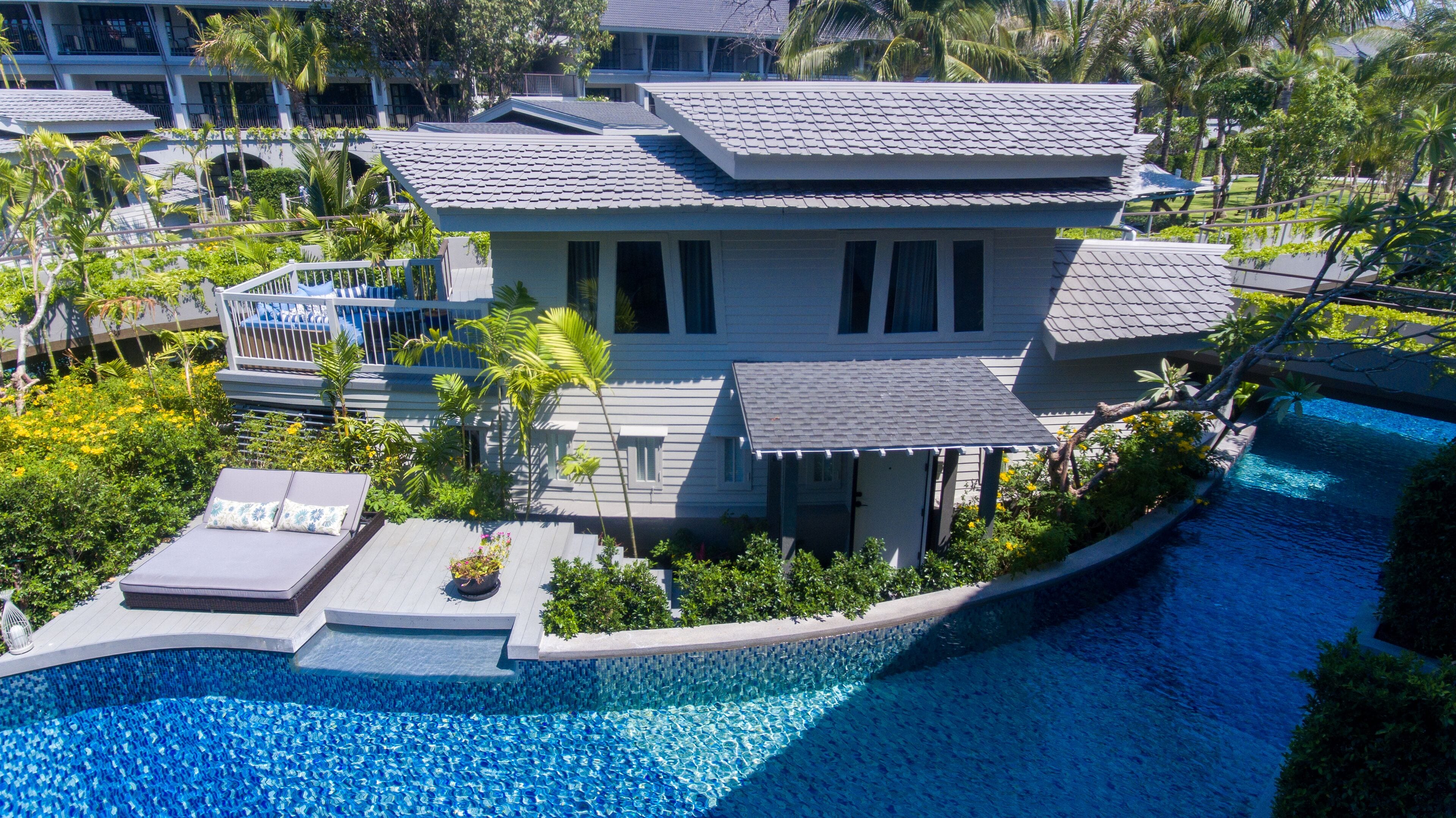 A modern house with a swimming pool, surrounded by lush greenery and palm trees.