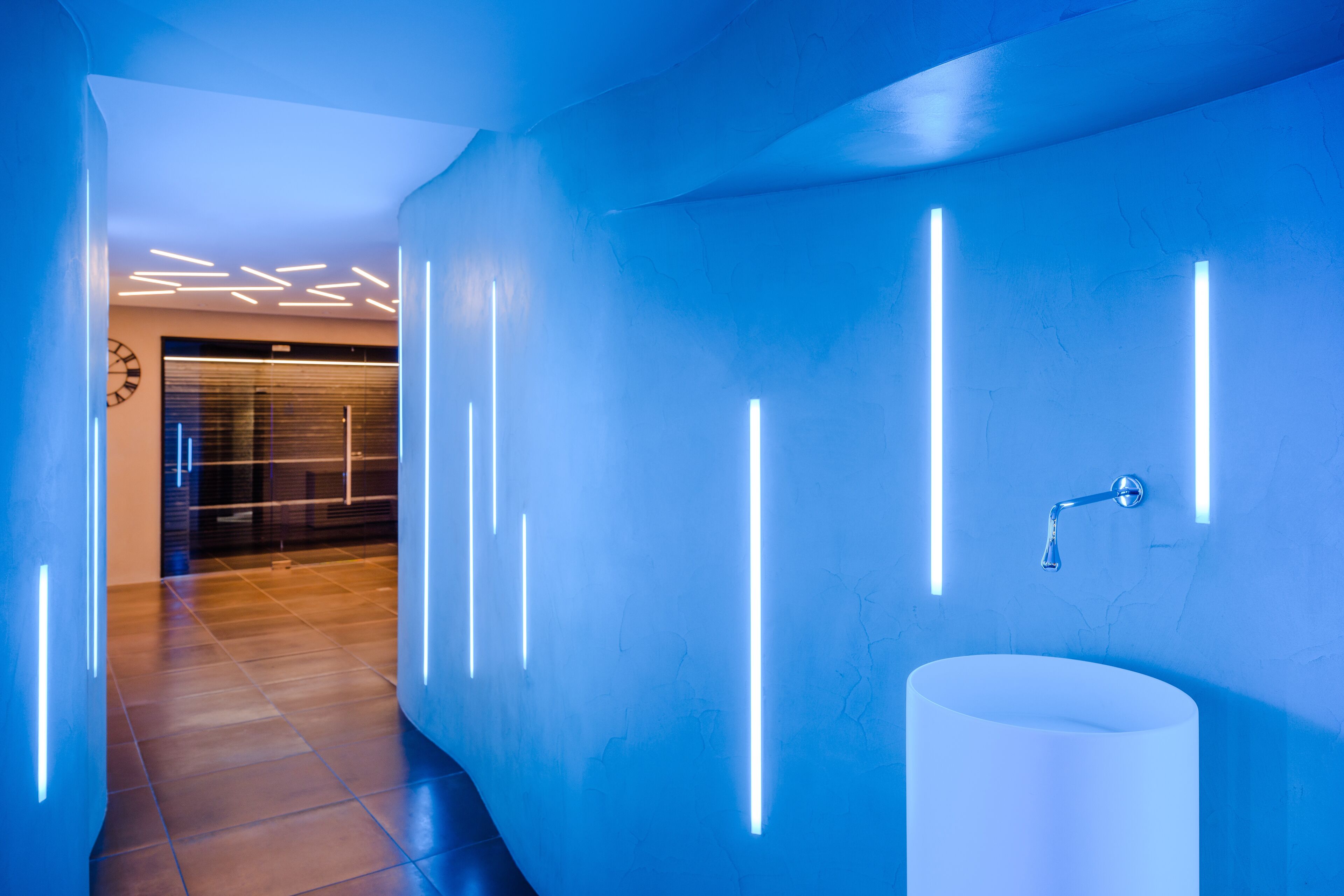 A modern bathroom with a white sink, blue lighting, and a tiled floor.
