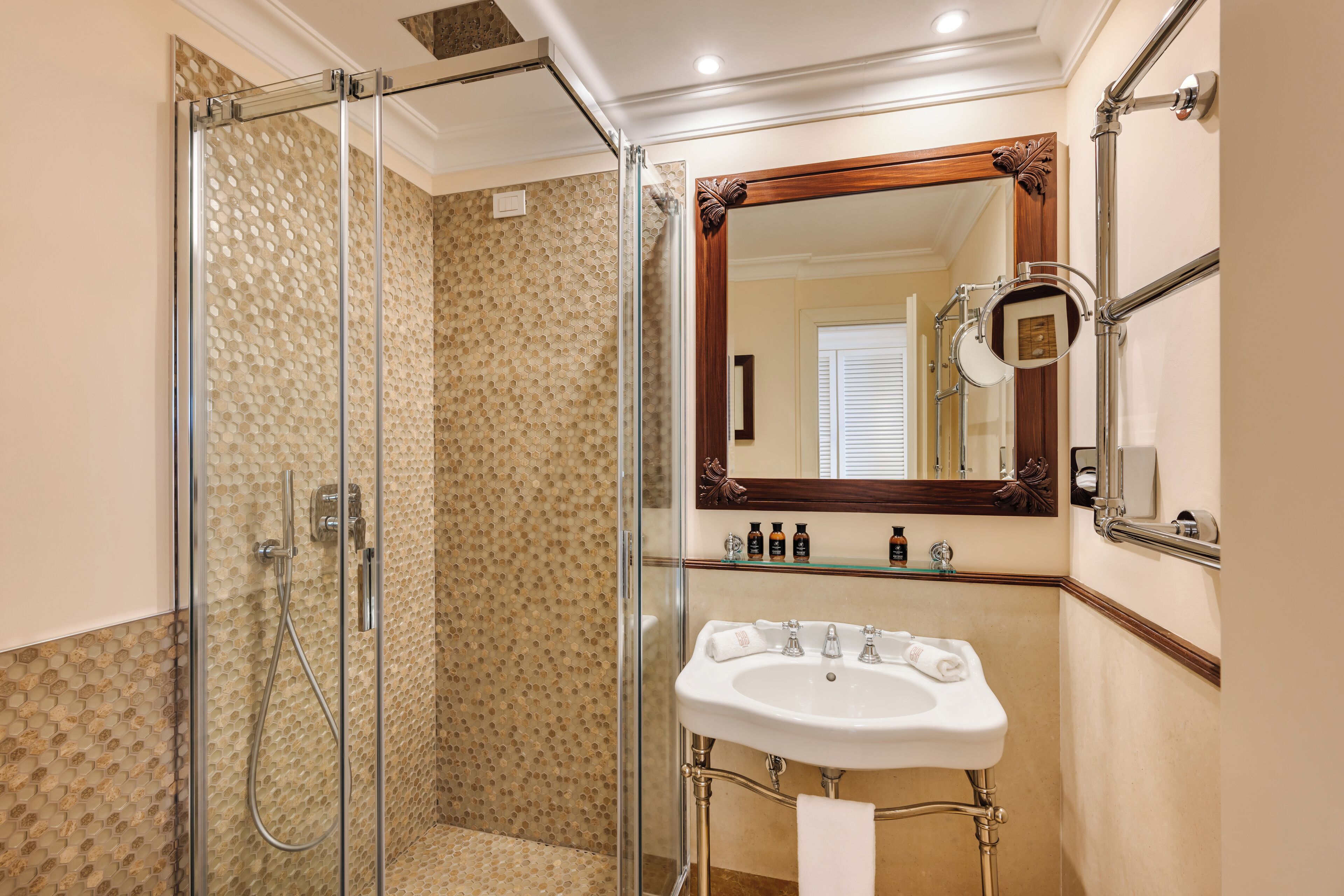 Un baño con cabina de ducha de vidrio, lavabo blanco y espejo con marco de madera.