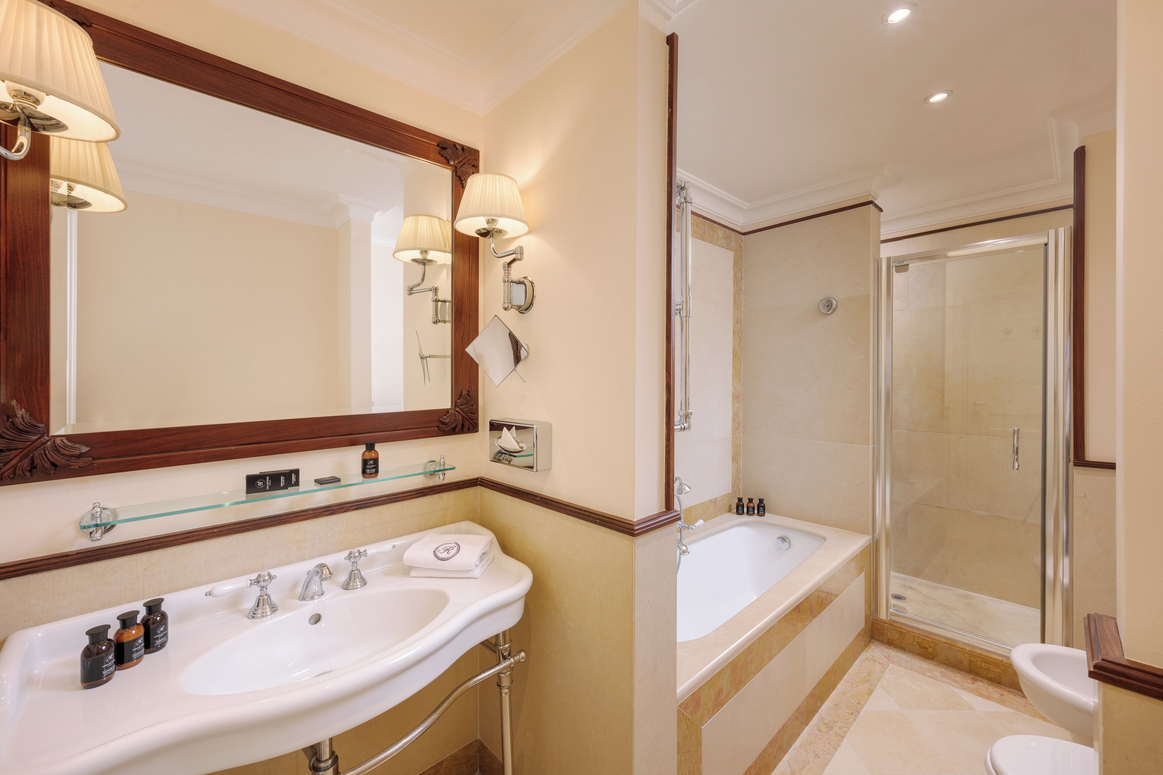 A bathroom with a large mirror, two sinks, a bathtub, and a shower.