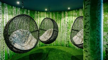 A room with three hanging chairs, each with a white cushion, against a green wall with a vertical pattern.