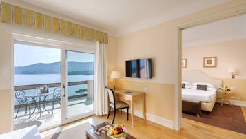 Una camera d'hotel con balcone, una scrivania, un letto, una TV e un'area pranzo con tavolo e sedie.