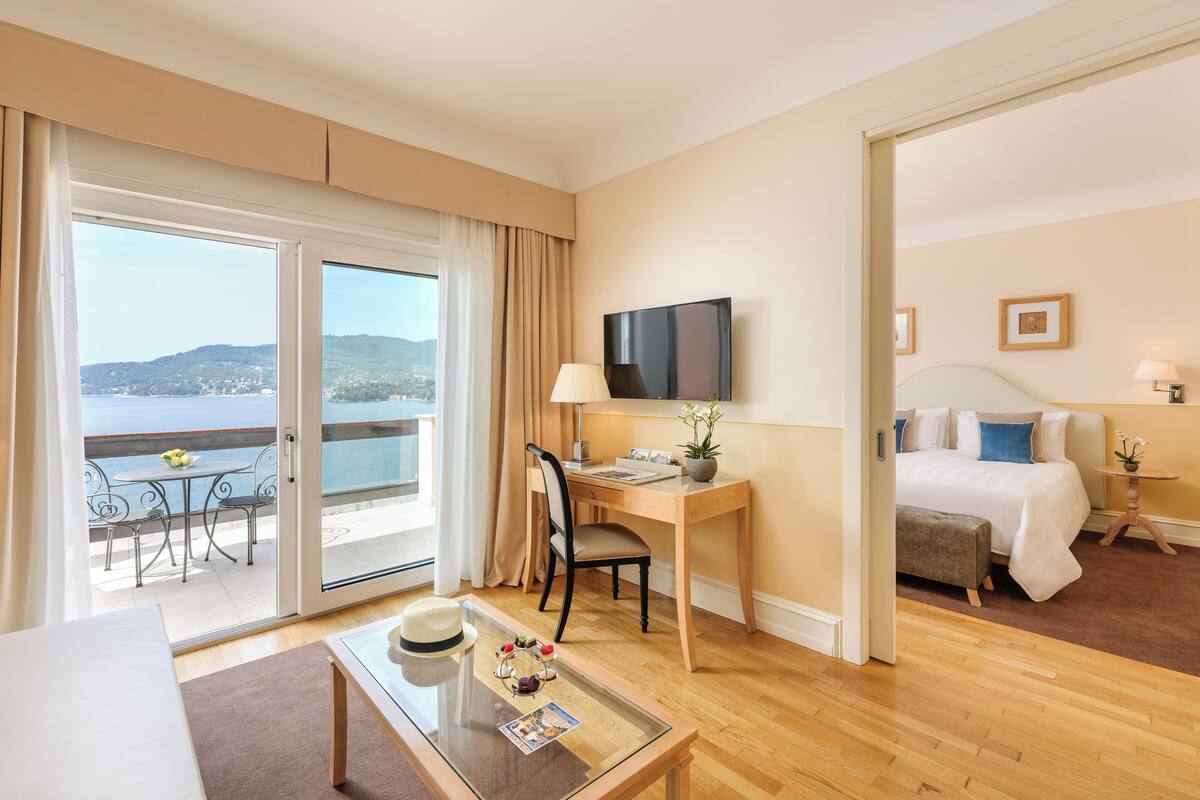 A hotel room with a balcony, a desk, a bed, and a television.