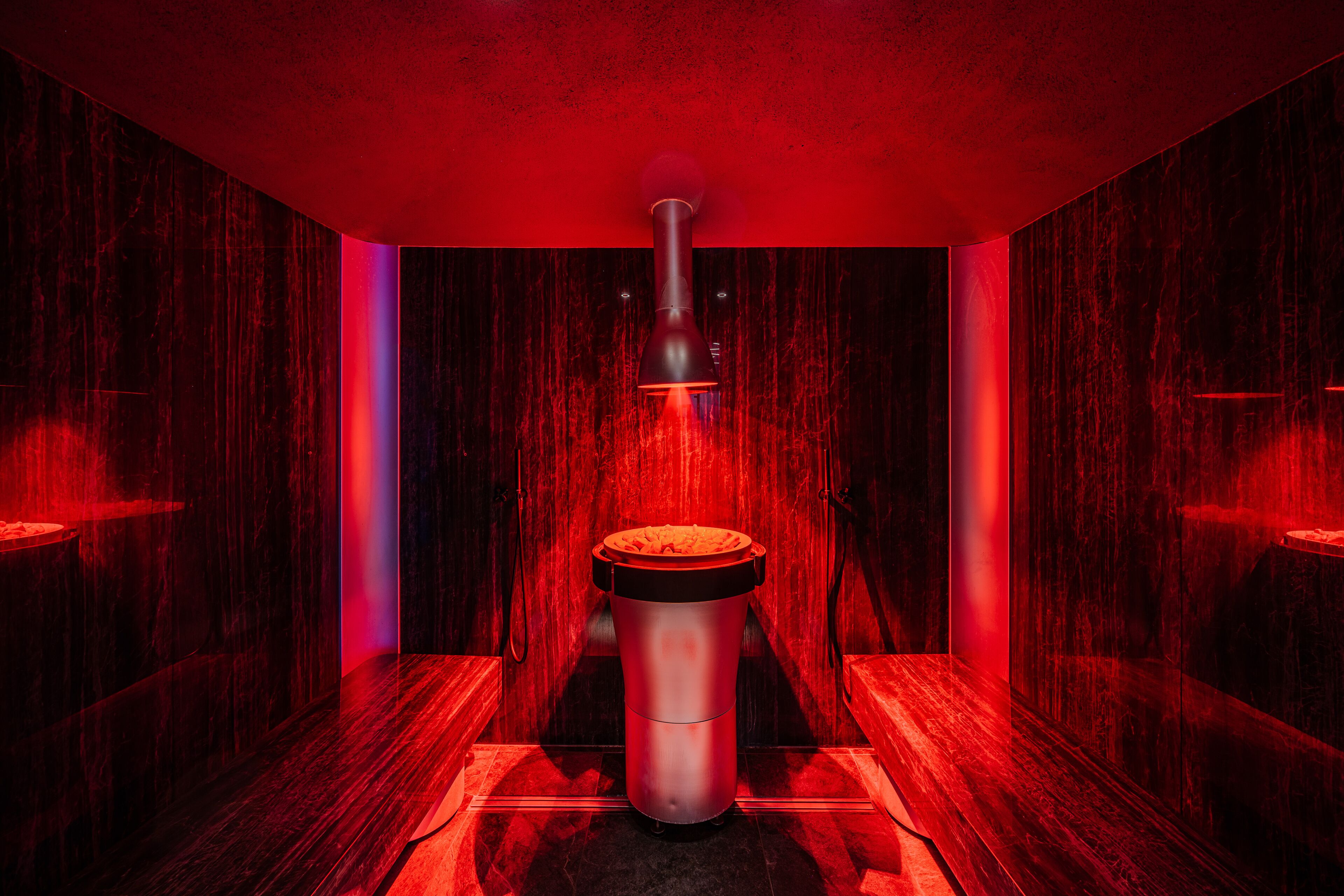 Un sauna con un calentador central que emite vapor, rodeado de paredes de madera y un suelo oscuro.